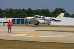 N300KP @ KOSH - While this Beech 55 Baron is landing for EAA AirVenture 2023 is a EAA volunteer busy to signal taxiing aircraft for another location on the field. - by lk1250
