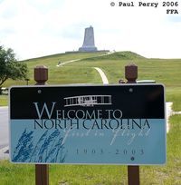  - The welcome sign at FFA, with the Wright Brother's Memorial in the background - by Paul Perry