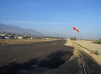  - New windsock at Runway 04 and new runway-parallel tiedown surfaced strip in preparation, the spaced clumps of dirt on the new surface show the bore holes for tiedown ring anchor insertions. Santa Clara River bed to the right - by Doug Robertson