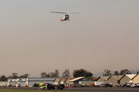  - Firebomber hovering over SZP FireBase with emptied sling load for replenishment. Fast turn-around time as Thomas fire here still burning (on shot date) just adjacent northern Santa Paula. Note smoky sky. - by Doug Robertson
